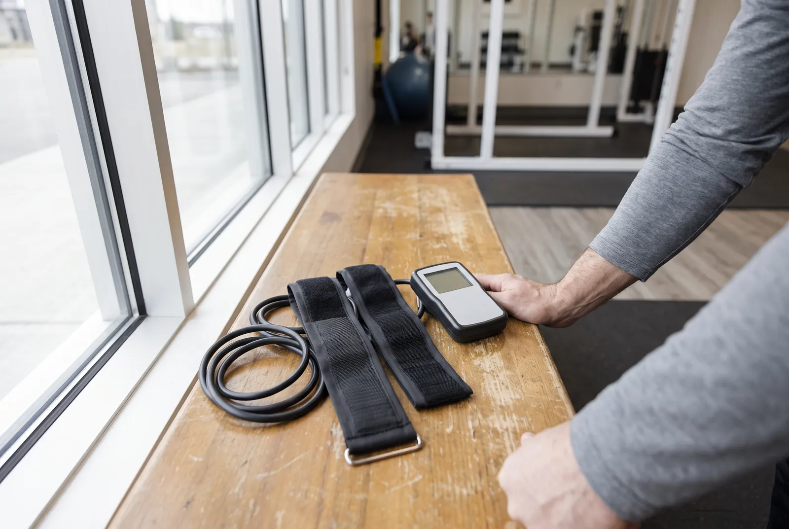 A blood flow restriction cuff system with tubing and a handheld device on a wooden bench