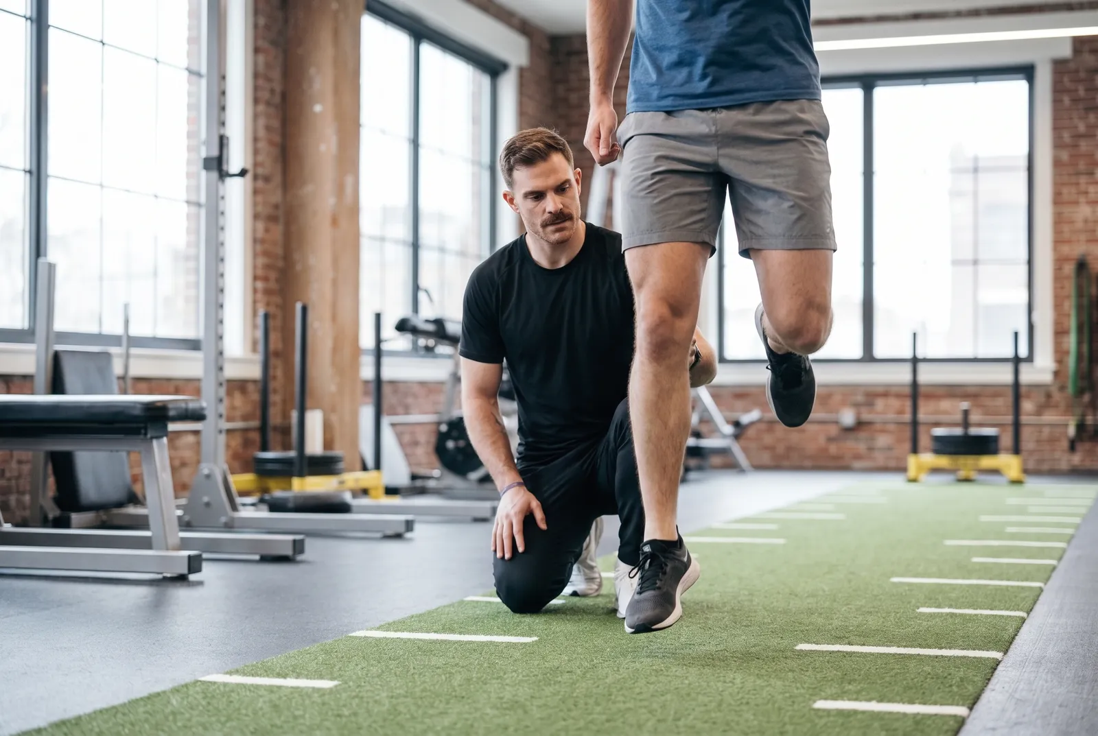 An athlete doing a single-leg hop test on turf while a physical therapist watches
